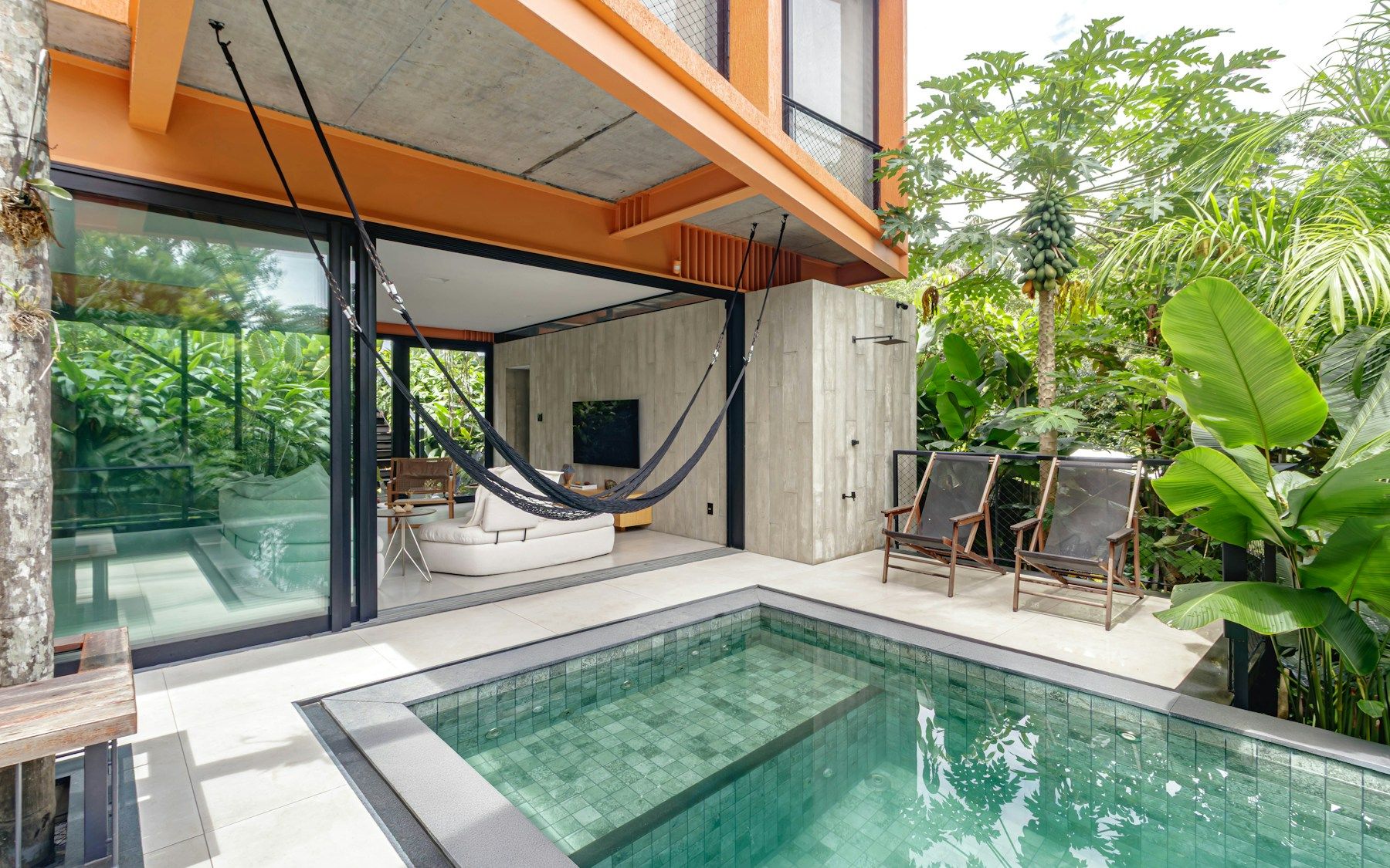 A white home opening onto a swimming pool and a leafy garden