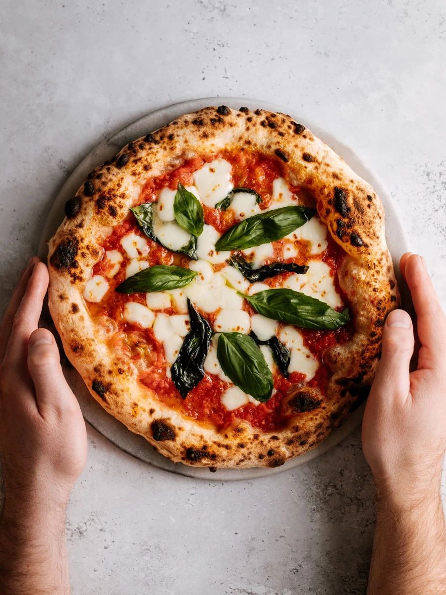 Fresh Neapolitan pizza with a puffed, lightly charred crust, tomato, mozzarella and basil.